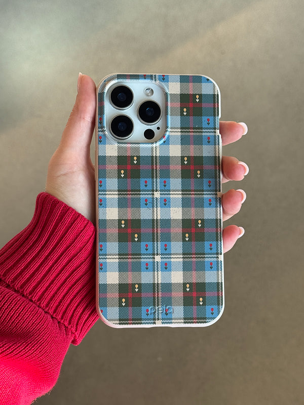 Hand holding a phone with the Plaid Picnic Phone Case by Pela, featuring a blue, green, and beige plaid pattern with small embroidered-style accents.